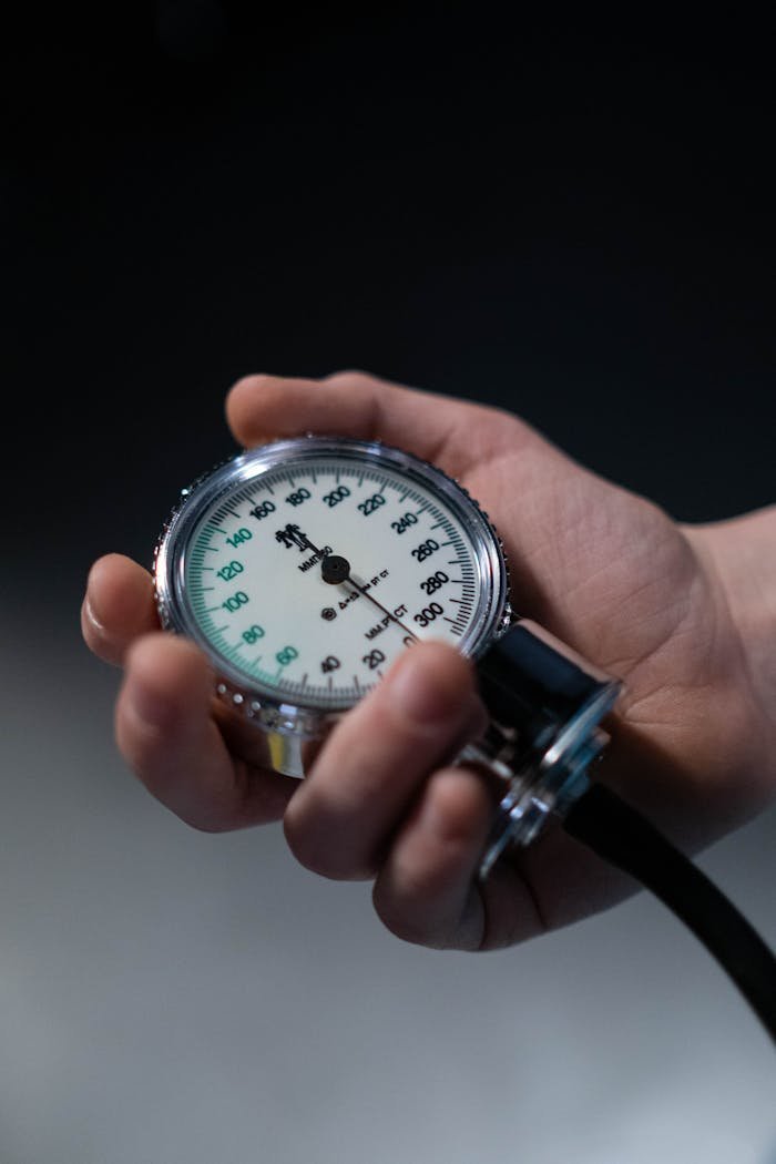A hand holding a sphygmomanometer showing blood pressure readings in a medical setting.